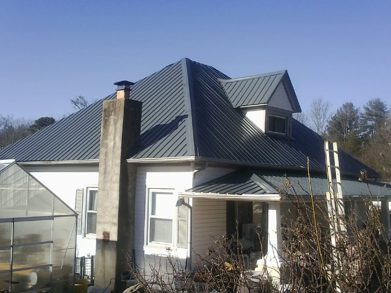 Dark blue standing seam metal roof on a white farmhouse with dormer — Slate & Tile Roof Repair by Roofing Brothers in Hersey