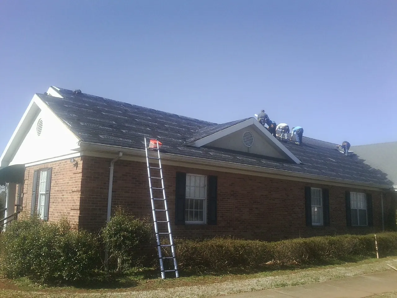 Crew tearing shingles off a brick ranch roof with a ladder set — Emergency Roof Repair work by our crew in Hersey