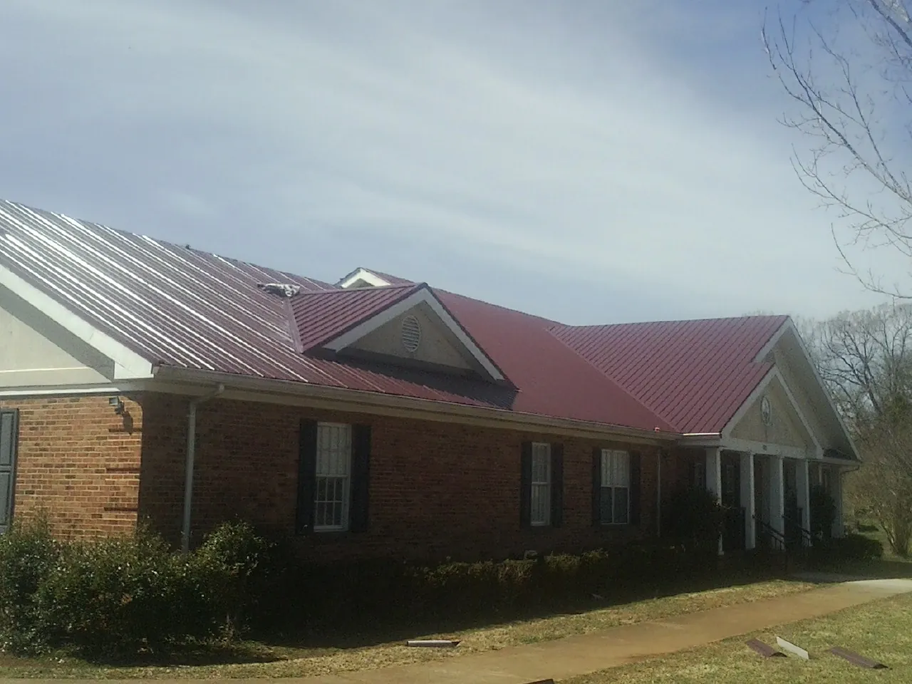 Red metal roof with gabled entries on a long brick building, from a Hail Damage Roof Repair job in Hersey