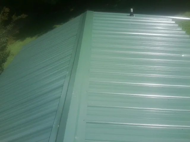 New green metal panels meeting at the ridge of a roof — Flat Roof Repair work by our crew in Hersey