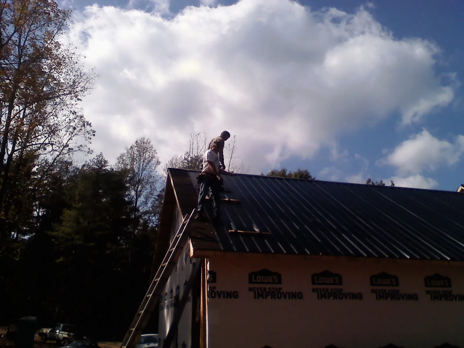Roofer fastening dark metal panels high against a cloudy sky, from a Roof Inspection job in Hersey