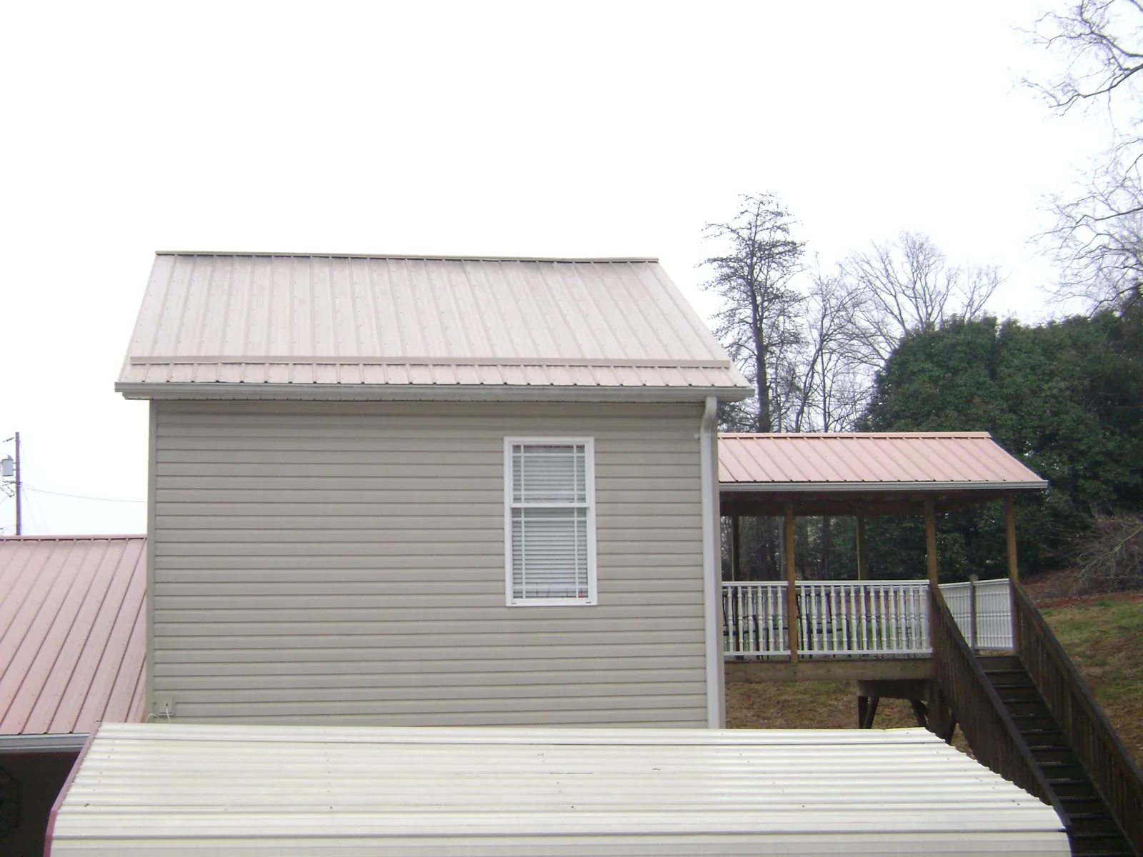 Tan metal roofs on a two story addition and attached porch, from a Roof Replacement job in Hersey